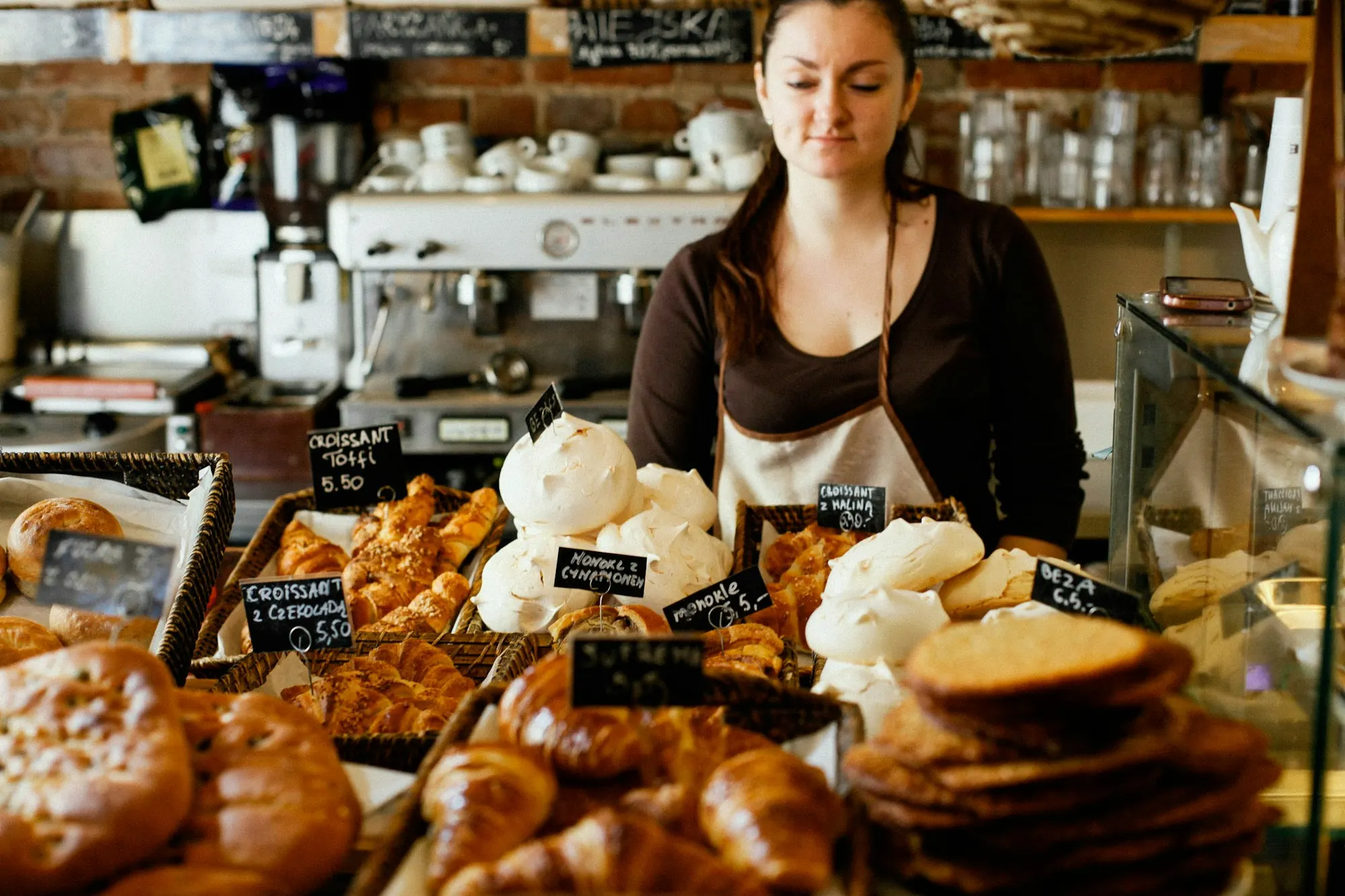 A baker behind a counter loaded with pastries and bread