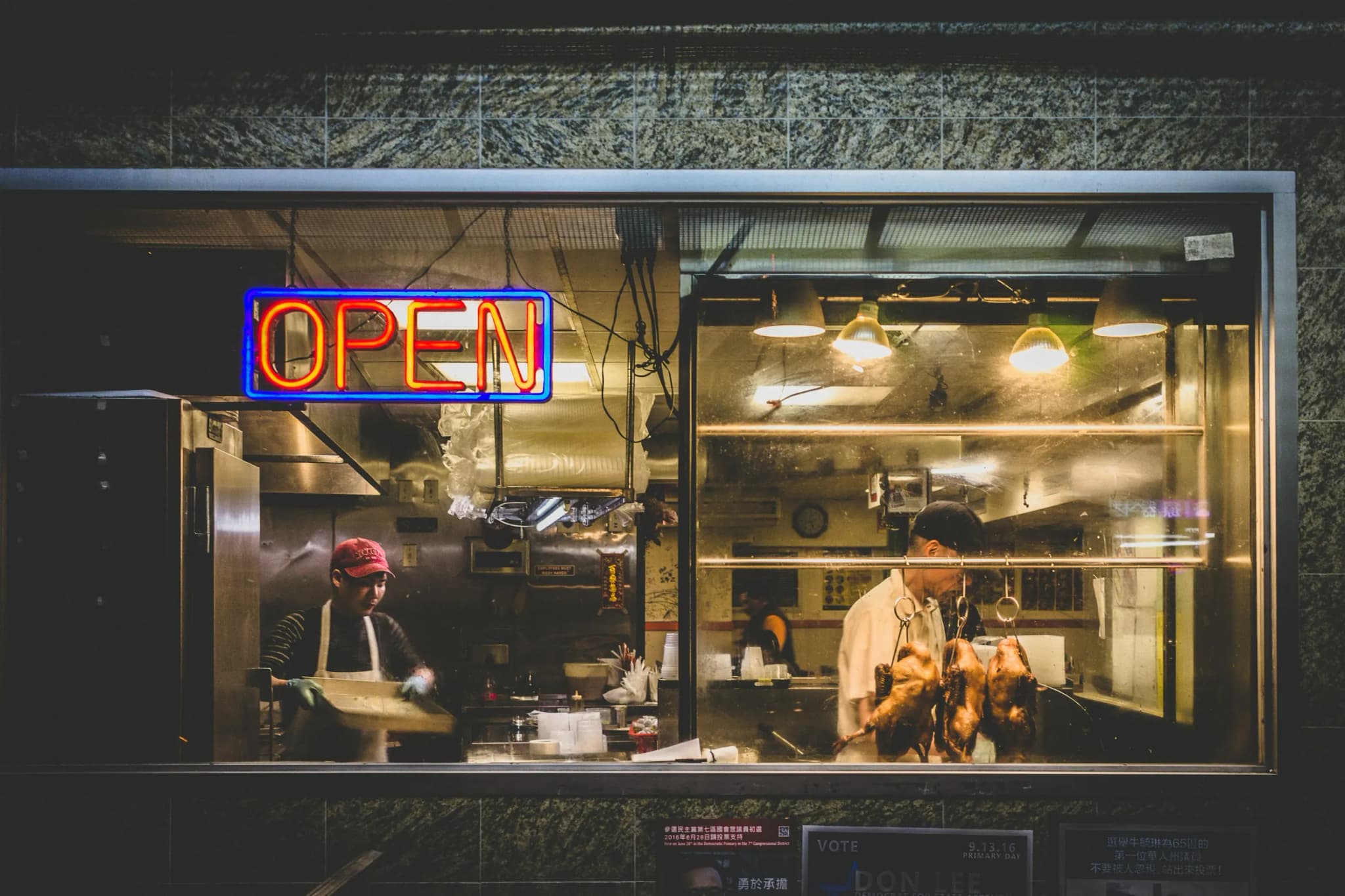 A kitchen still working behind a lit OPEN sign late at night