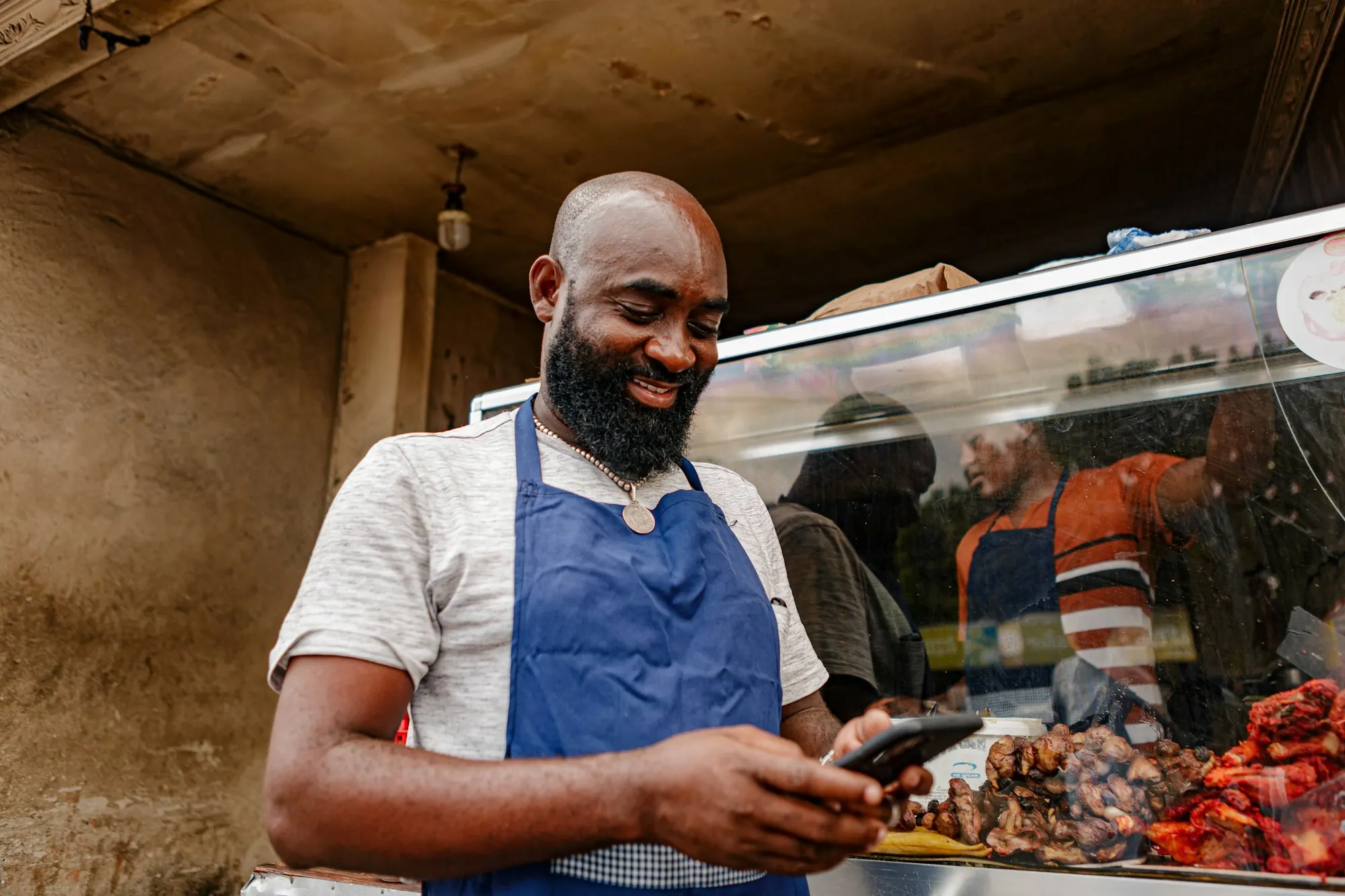 A shop owner in an apron checking his phone behind the counter